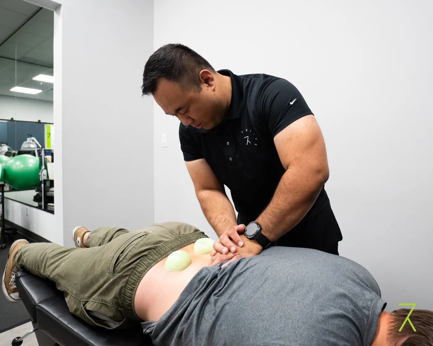Chiropractor performing instrument-assisted soft tissue treatment on a patient's lower back at Revive Rehab